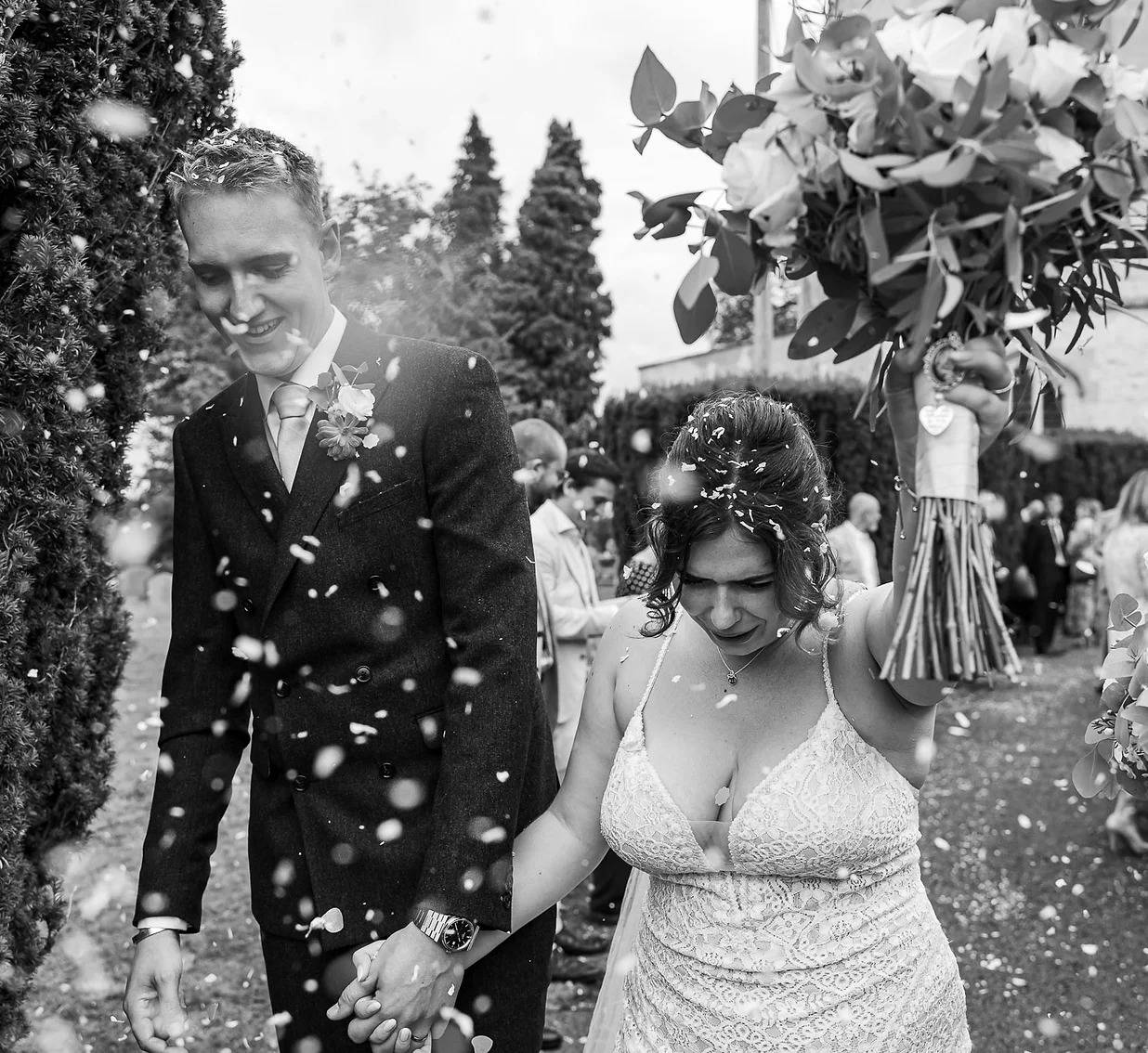 bride holds bouquet in air as they walk through a lot of confetti
